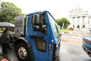 A Mack electric refuse truck in front of the Pennsylvania capitol building