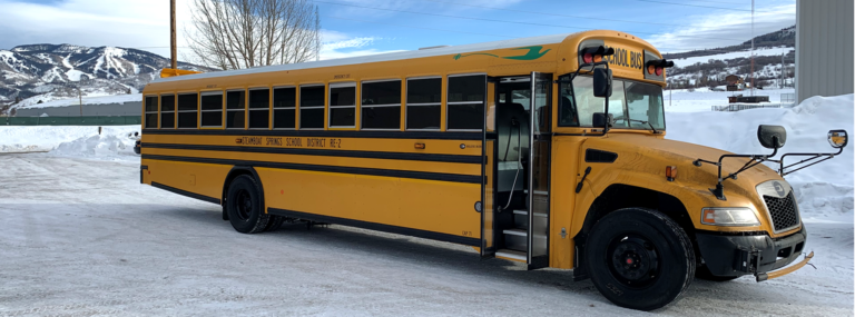 An electric school bus in front of a school in the Colorado mountains during winter.
